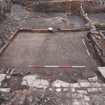Remains of a flagged passageway in the foreground which provided external access to the cellar dwelling © Copyright ARS Ltd 2022